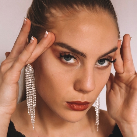 Photo of Candace posing with her hands on her temples; wearing dramatic makeup, her hair slicked back, a black robe, and diamond drop earrings.