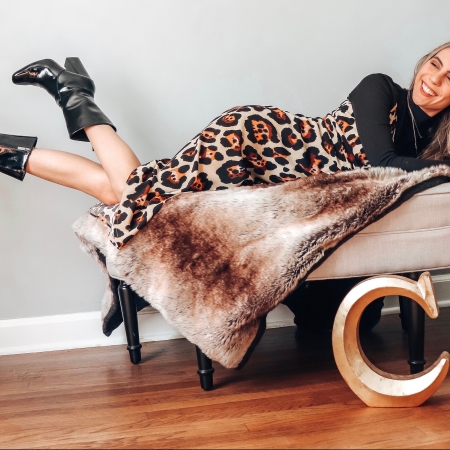 Candace lounging happily of a faux fur blanket in a leopard print dress, black turtleneck, and black calf boots.